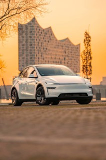White electric car in front of a modern architectural backdrop at sunset, Tesla New Model Y,