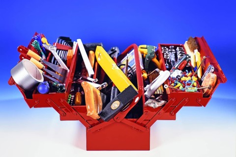A red toolbox with tools, hammer, screwdriver, adhesive tape, folding rule, pliers, chisel, plane,