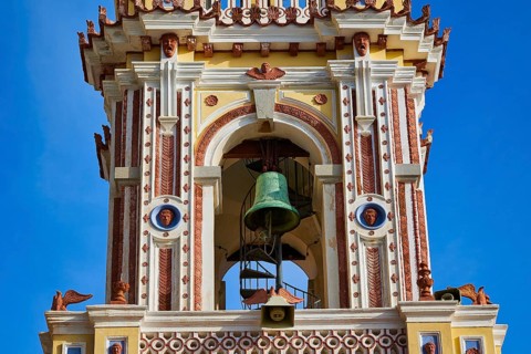 Detailed view of a baroque decorated church tower with visible bell under a blue sky, Holy Week,