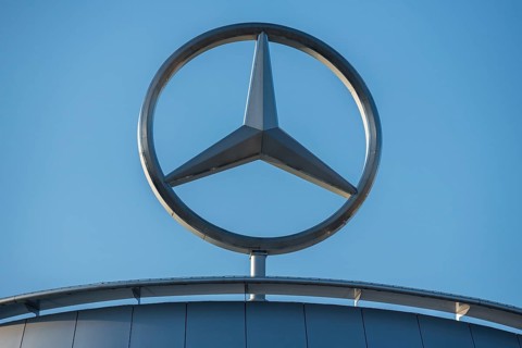 Close-up of the Mercedes star on a metallic building in front of a clear sky,