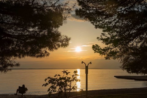 Quiet sunset by the sea, framed by silhouettes of trees, man sitting on the beach, Starigrad,
