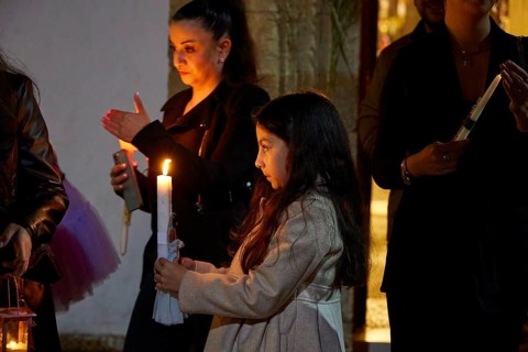 Two woman stand in the candlelight, one of them holding a candle and gazing silently at the light