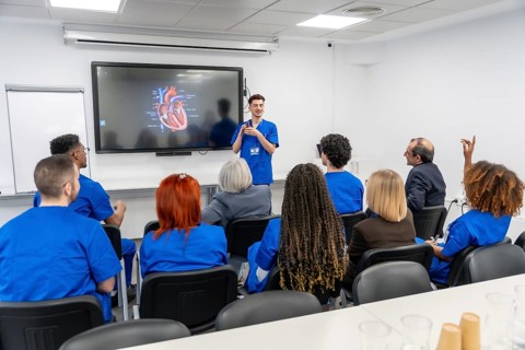 Medical professional standing, explaining human heart anatomy to a diverse group of students in