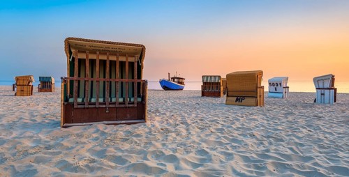 Beach chairs and fishing trawlers on a fine sandy beach at sunrise, Baltic resort Heringsdorf,