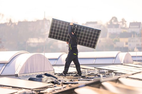 Worker lifts a solar panel on a roof in an urban area in sunny weather, PV installation at OBI
