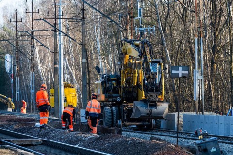 Railway construction crew in high-visibility gear working on tracks alongside a yellow road-rail
