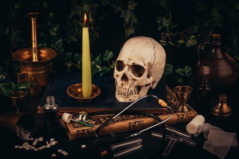 A skull with a candle on antique books, framed by medical tools in a dark atmosphere
