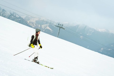 Georgian skier boy teenager skiing alone on snowy beginner slope with ski lift chairs passing above