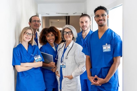 Diverse team of doctors and nurses in scrubs and lab coats standing in a bright hospital hallway,