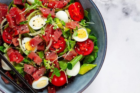 Salad with fresh tuna, cherry tomatoes and quail eggs and avacado, served with chopsticks