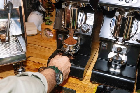 A barista grinds fresh coffee beans into a portafilter using a professional espresso grinder. The