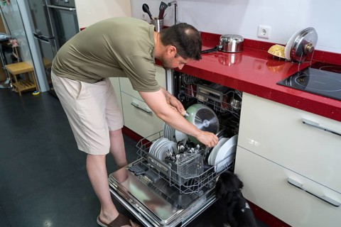 A man in casual attire loads dishes into a dishwasher in a modern kitchen. The countertop features