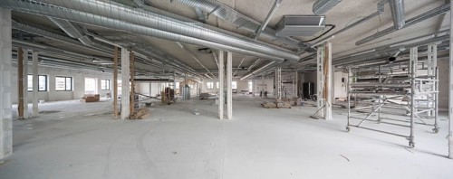 A large office interior is under renovation, featuring exposed industrial ducts and scaffolding.