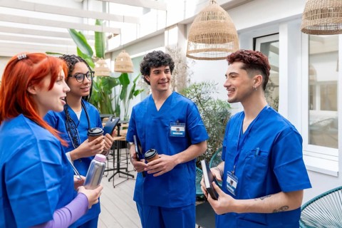 Group of young medical students in blue scrubs and stethoscopes smiling and holding drinks while