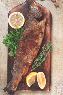 Fried rainbow trout, with herbs and citrus fruits, on a wooden chopping board, top view