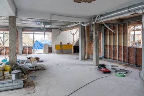 Indoor commercial space under renovation featuring concrete pillars, new brick walls with metal