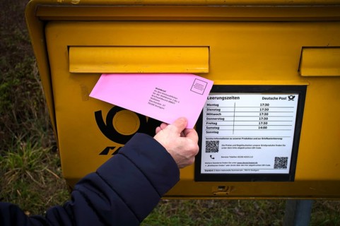 Woman throws ballot letter into mailbox, ballot envelope, bright red, pink, postal ballot, official
