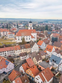 View of a small town with a historic church in the centre, surrounded by red roofs and countryside,