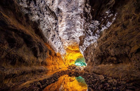 Lava tunnel, illuminated lava cave with perfect reflection in an underground lake, Cueva de los