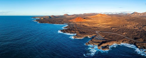 Coast with lava fields, volcanic landscape near Los Hervideros with red volcano Montaña Bermeja, in
