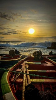 Colorful fishing boats on the shore with ropes and setting sun over the sea, dramatic coastal