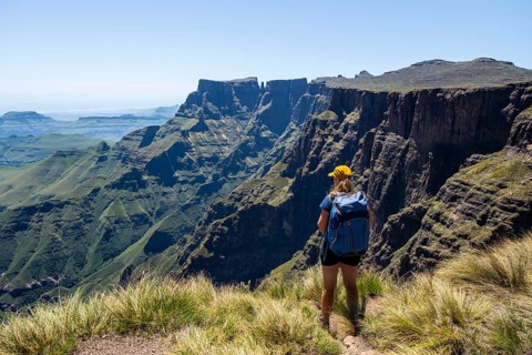 Young hiker looking at the impressive mountains and cliffs of the Drakensberg Mountains, hiking