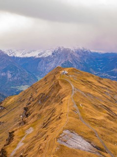 A path winds over a brown mountain ridge with snow-capped peaks in the background, Alpen Tower,