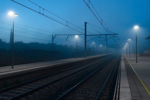 A serene railway station engulfed in fog under the dim glow of street lights, with empty tracks
