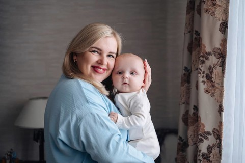 A joyful mother lovingly holds her infant son near a window, enveloped in soft natural light. The