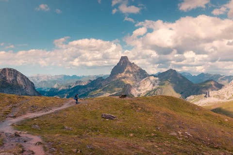 A lone hiker walks along a scenic trail with a stunning mountain peak in the Pyrenees. The
