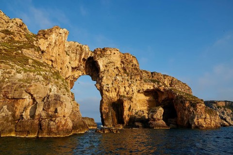 An impressive rock arch rises from the sea, morning light, Tsichli Babas islet, Navarino Bay,