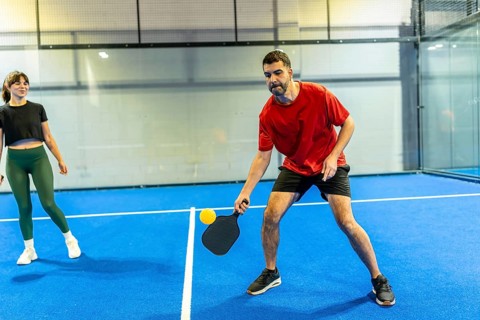 Two players competing in a dynamic indoor pickleball match on a blue court with white lines,