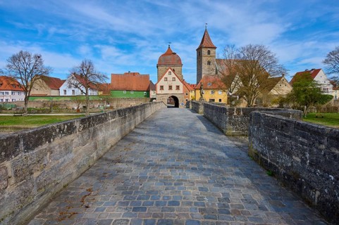 View along a historic stone bridge with cobblestones to a village with church and city gate,