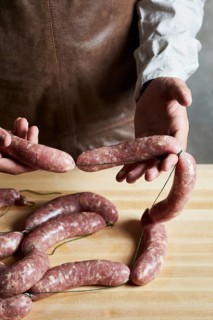 Butcher carefully handles fresh sausages, preparing them on a wooden surface. The image showcases