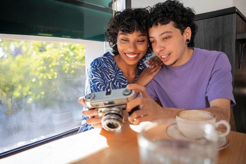 A happy multiethnic LGBTQ+ couple sits together in a cozy cafe, sharing a joyful moment while