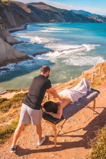View from above of a massage in nature on the coast near the sea, masseuse with face mask in the