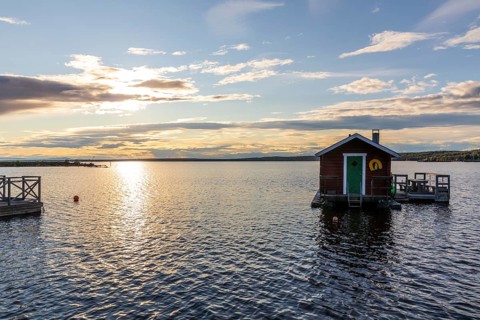 Small wooden house with seat on the water with boat dock, evening mood with sun and clouds on Lake