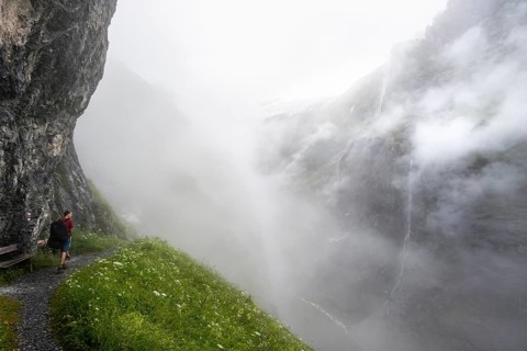 Mountaineer hiking on a hiking trail on a steep rock face, hiking to Berghaus Bäregg, cloud-covered