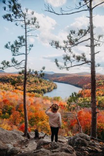 A person stands on a rocky overlook in Quebec, Canada, admiring a picturesque autumn landscape. The