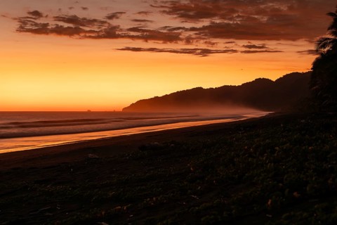 After sunset, the deep red sky glows above palms and ocean spray with views of Corcovado National