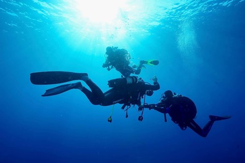 Three divers together underwater at a decorative stop, surrounded by sun rays and blue water, Giens