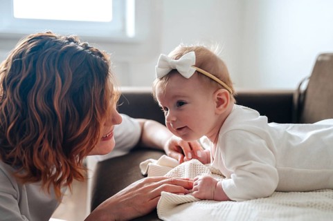 A mother lovingly gazes at her newborn baby girl, who is dressed in a soft white onesie with a bow