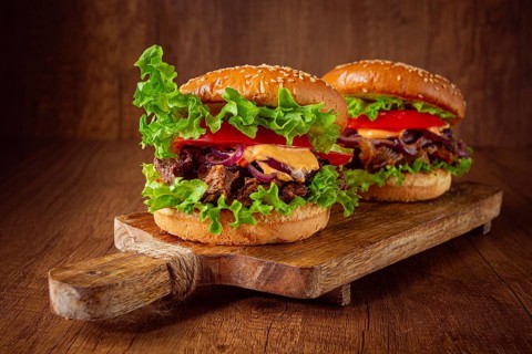 Two burgers are stacked high with fresh lettuce, tomato slices, grilled onions, and a savory sauce.