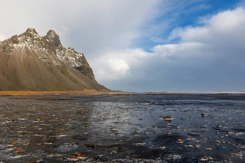 Teared water on lava sandy beach against mountain backdrop, sea, snow, winter, Stokksnes,