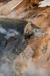 Steaming stream between colourful rhyolite mountains and snowfields, Hveradalir geothermal area,