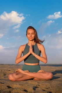 Woman in padmasana lotus pose on sandy beach at sunset, hands in namaste, embodying tranquility and