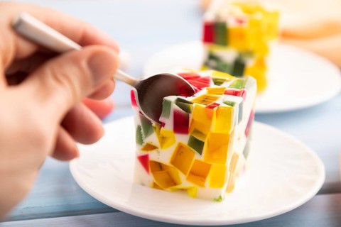 Colored Fruit and milk jelly with hand on blue wooden background and orange linen textile, side