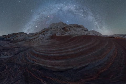 Stellar Milky Way galaxy arching above the swirling, layered rock formations of a Utah desert