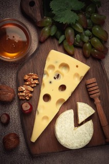 Cheese with big holes, emmental, maasdam, brie cheese, on a cutting board, with grapes and honey,