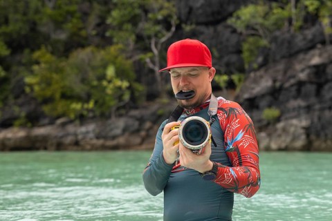A photographer in a red cap takes pictures in Raja Ampat, Indonesia Turquoise water and lush